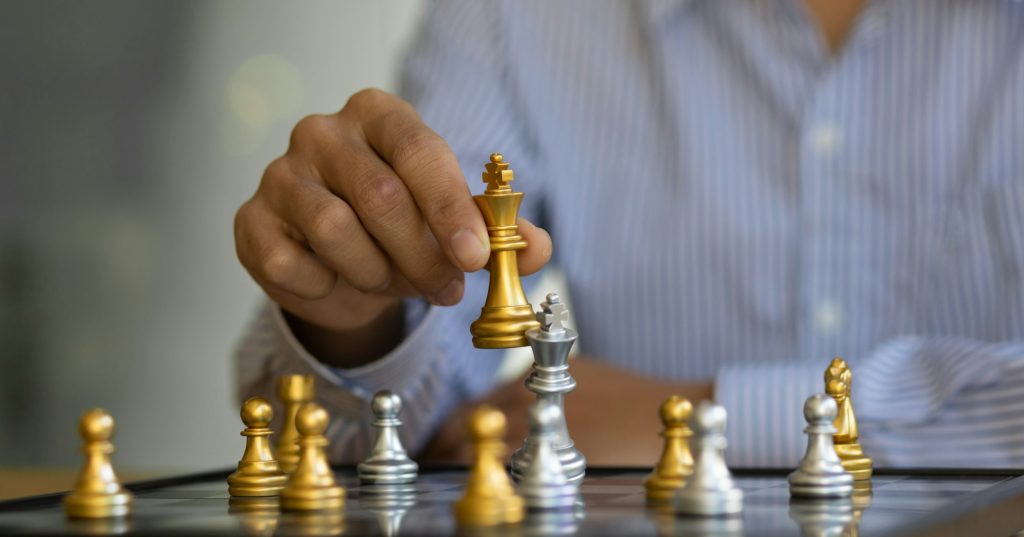 Businessman moving gold Chess King figure and Checkmate opponent during chessboard competition.